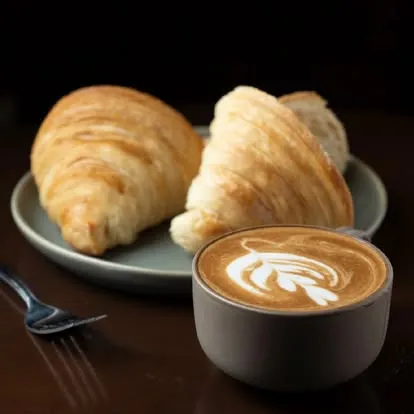 Two croissants beside a cup of coffee with leaf latte art.